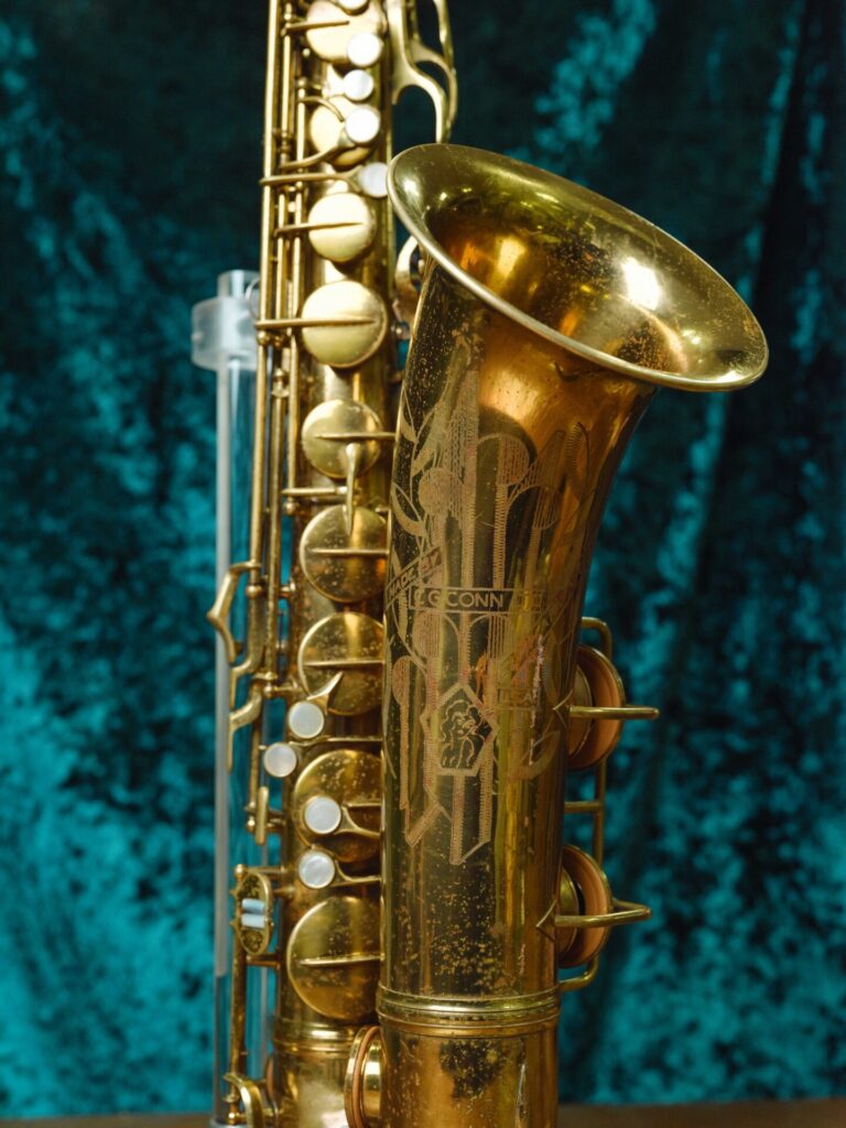 A close-up of a vintage brass saxophone with engraved details on the bell, set against a textured teal fabric background—a timeless piece ready for a new era at Meridian Winds.