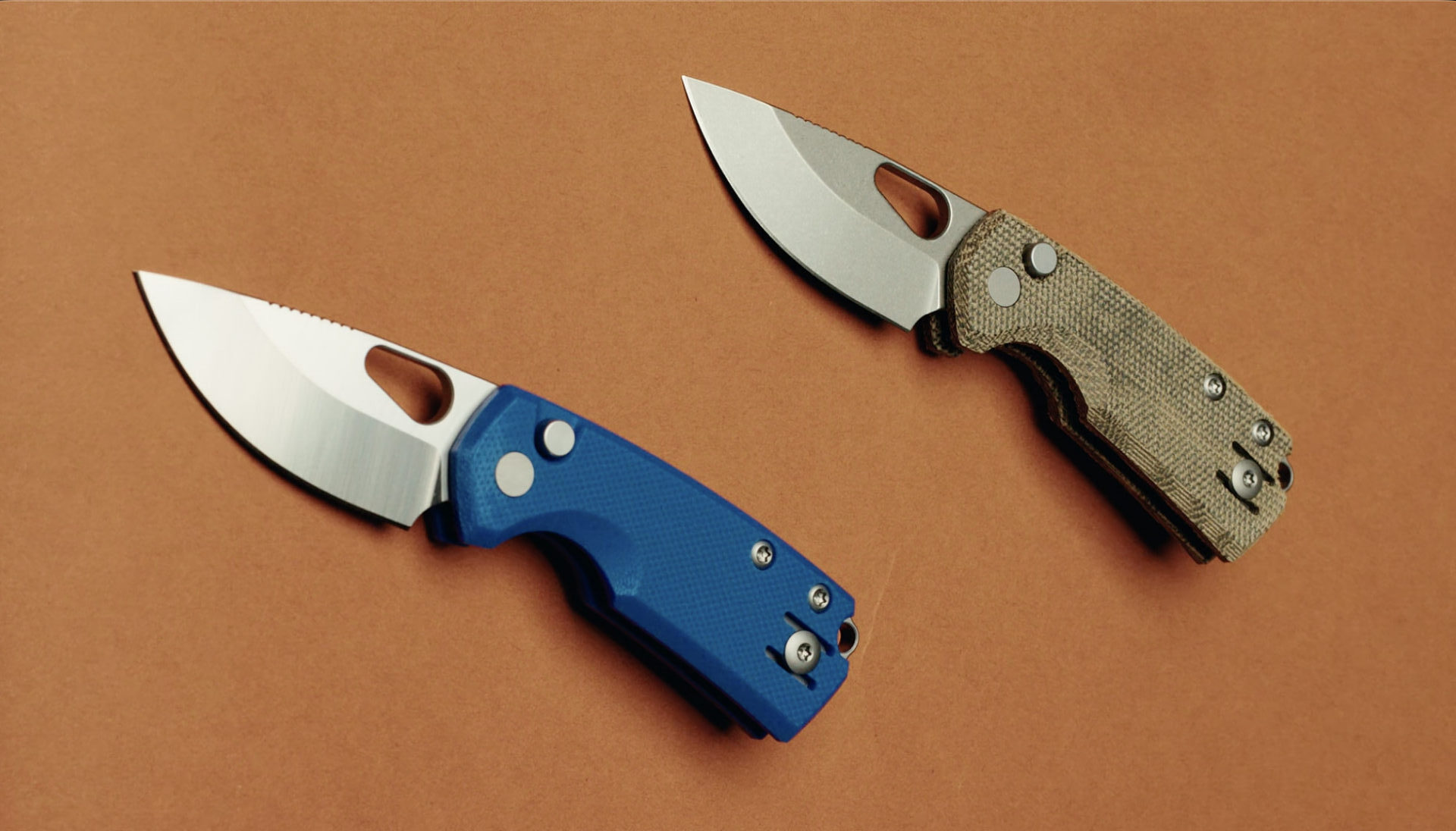 Two folding GiantMouse Knives with textured handles—one tan, one blue—are displayed on a brown background. Both knives have partially open stainless steel blades, perfect for showcasing in your next social video.